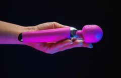 Eine Hand hält einen pinken Massagestab vor einem schwarzen Hintergrund