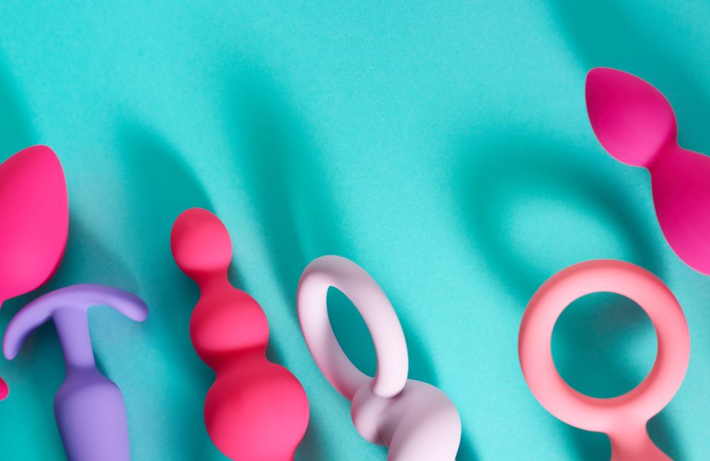 Verschiedene bunte Dildos liegen auf einem hellblauen Untergrund